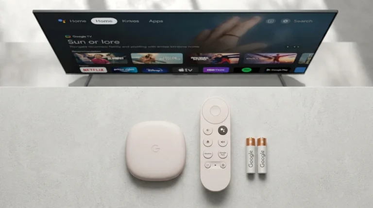 Google TV Streamer Voice Remote and device on a surface with a Google TV home screen visible on a TV in the background